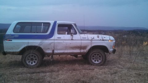 1979 Ford Bronco - This 1979 Ford Bronco, seen from the side, is covered in mud and parked in a dry, grassy field under an overcast sky.