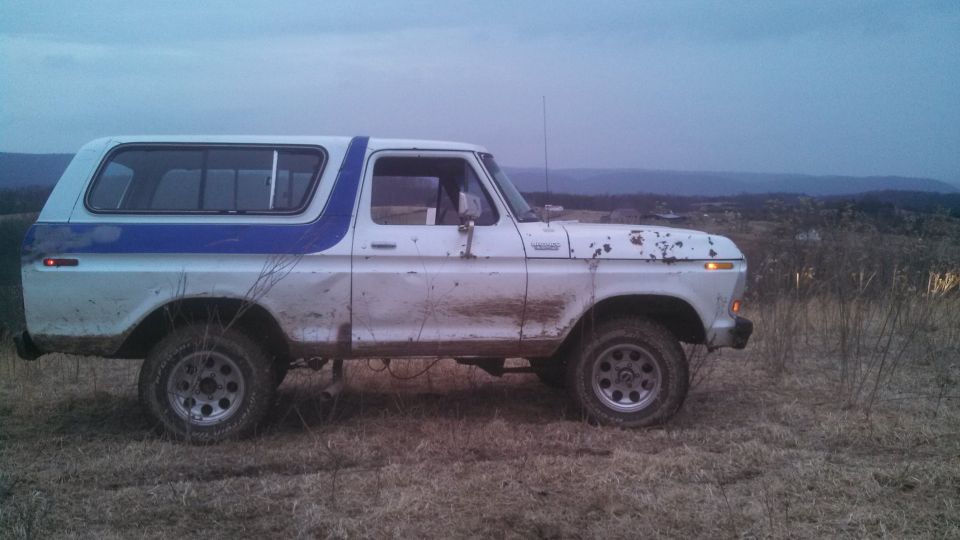 Side view of a white and blue 1979 Ford Bronco parked in a field