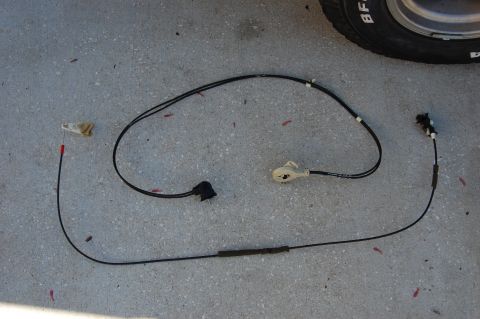 1994 Ford Bronco - A detached vehicle door latch cable assembly lies on a concrete surface.