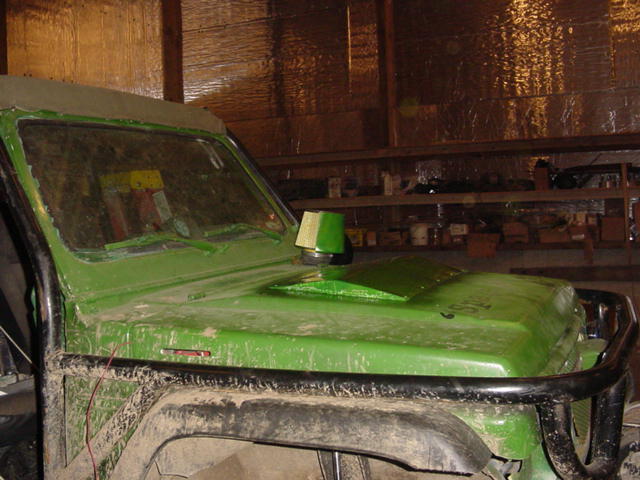Green off-road vehicle with custom hood scoop and roll cage, parked indoors