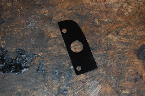 1994 Ford Bronco - A black metal bracket with a large central hole and two smaller holes is shown on a textured wooden surface.