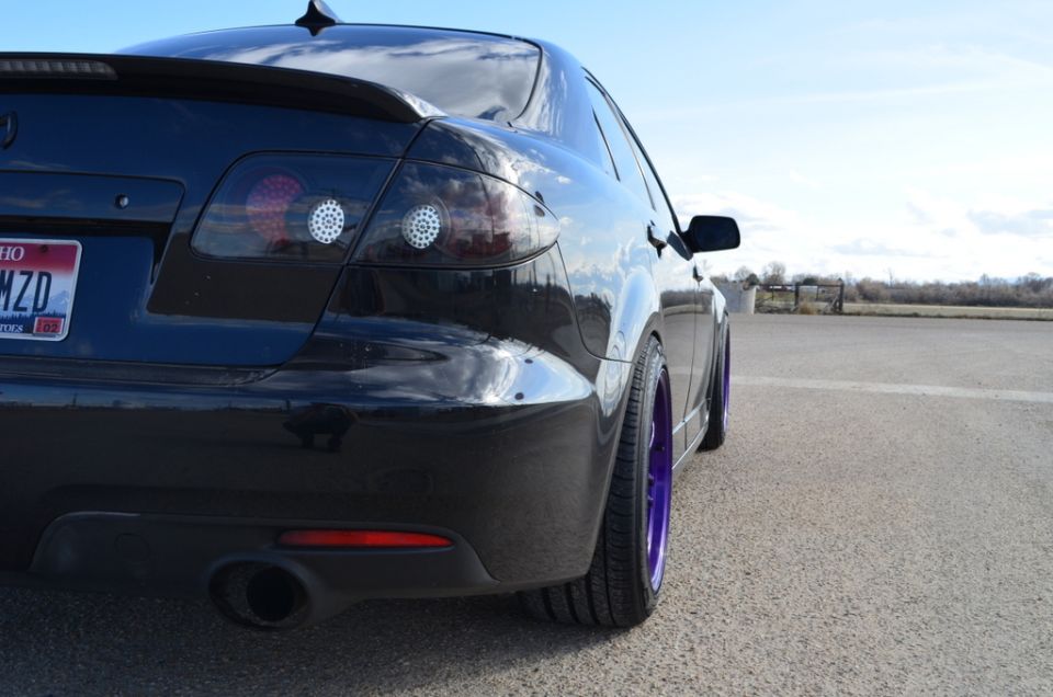 Black sedan, rear quarter view, purple wheels, spoiler, tinted taillights, license plate reads 'OH MZD'