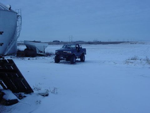 1992 Ford Bronco - A 1992 Ford Bronco sits in a snowy field, its soft top removed, with a grain silo to its left.
