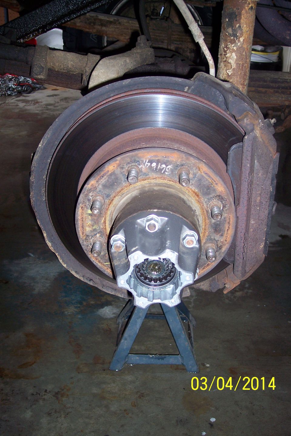 Close-up of a vehicle's front wheel hub and brake rotor, supported by a jack stand