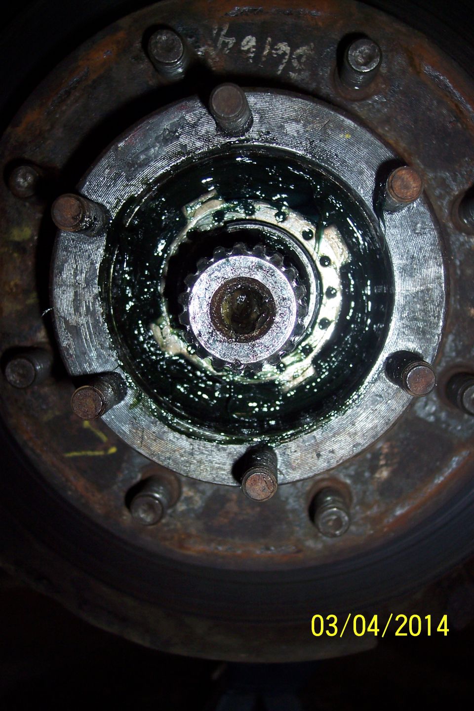 Close-up of a greasy wheel hub with multiple studs and a splined axle shaft
