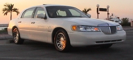 2002 Lincoln Town Car - A white 2002 Lincoln Town Car is parked near the water with palm trees in the background during sunset.