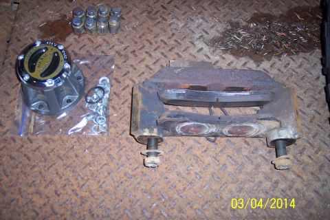 1973 Ford F-250 - Various vehicle parts including a brake caliper, lug nuts, and a hub assembly are laid out on a textured surface.