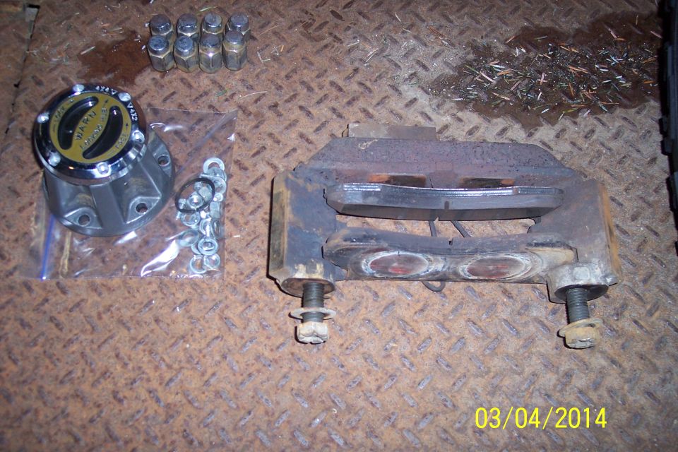 Brake caliper assembly, lug nuts, and a hub assembly with hardware on a metal surface