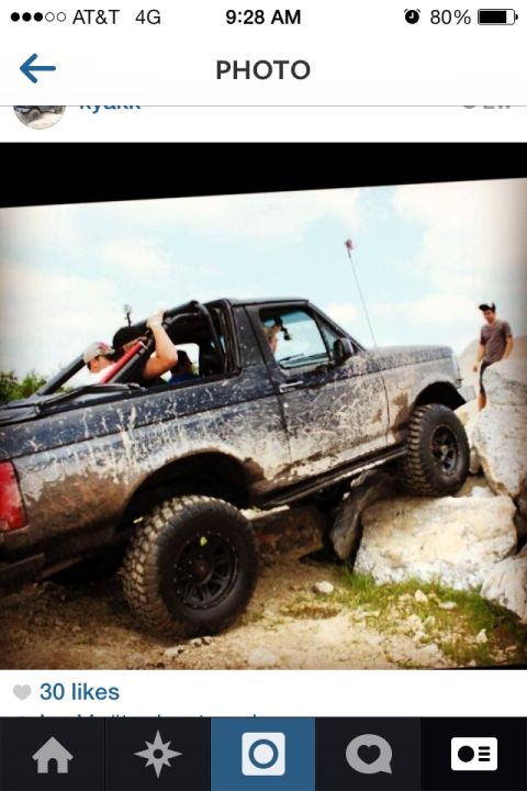 1995 Ford Bronco - A black Ford Bronco navigates a rocky terrain, covered in mud from off-roading.