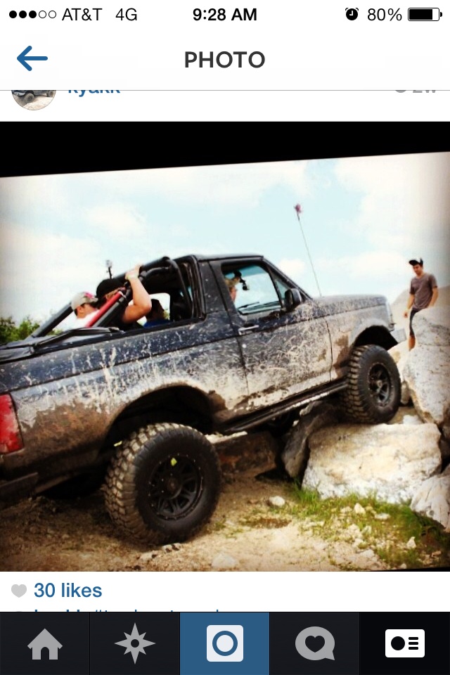 Mud-covered black Ford Bronco with a lifted suspension, off-roading over rocks