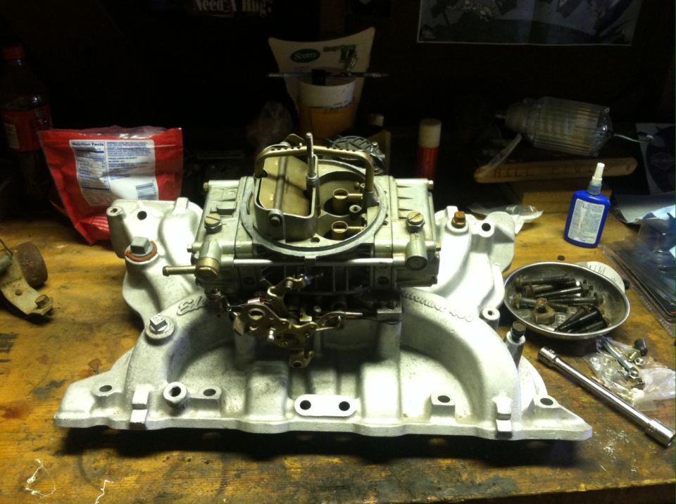 Carburetor and intake manifold on a workbench with tools and a bag of chips