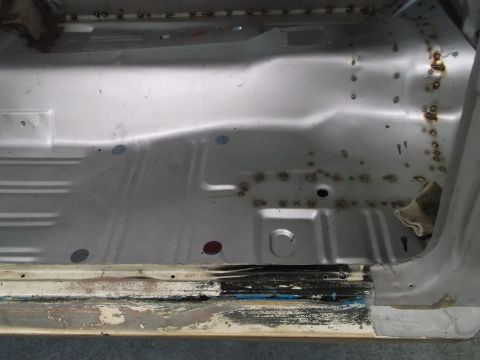 1967 Ford Mustang - The interior floor pan of a vehicle shows signs of rust and repair work, with visible welds and stripped paint.