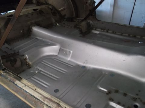 1967 Ford Mustang - Bare metal interior floor pan of a 1967 Ford Mustang undergoing restoration, showing seat mounting points and structural reinforcements.