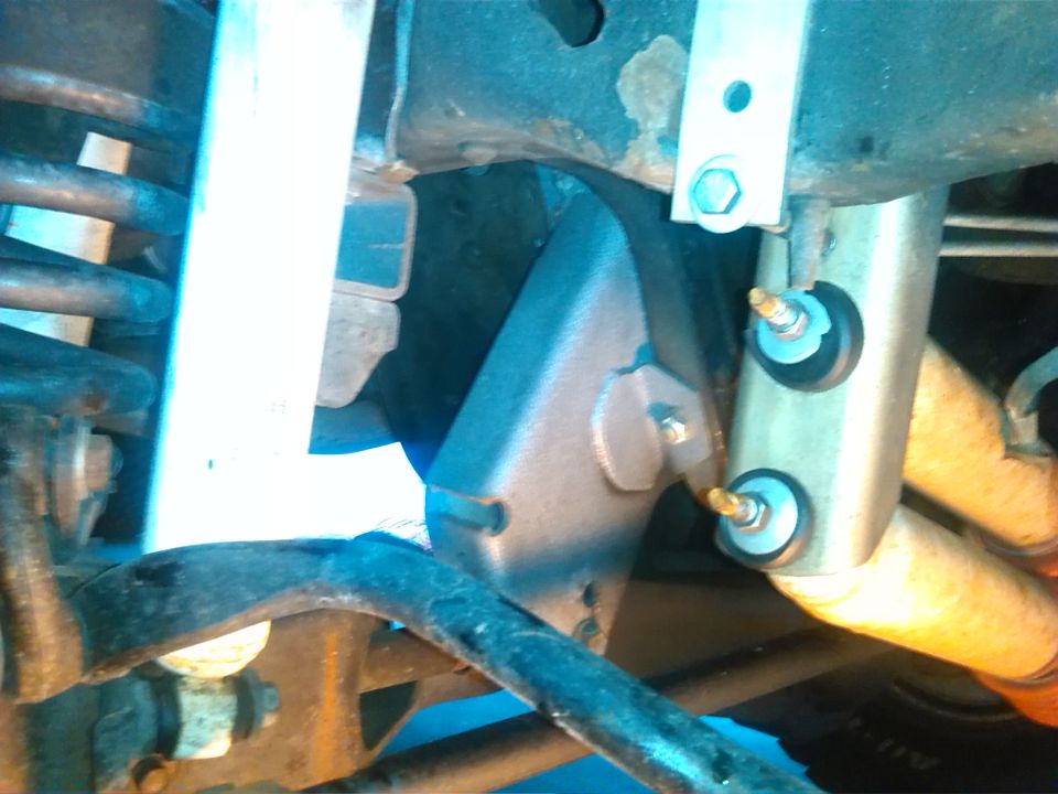 Close-up of a vehicle's rear suspension with shock absorber and springs visible. A metal bracket is attached to the frame