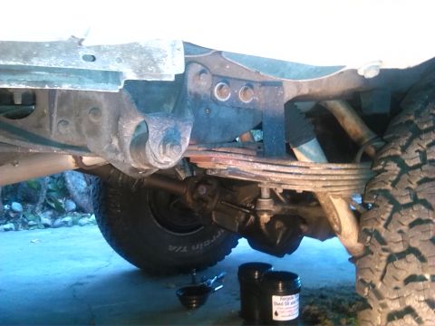 1992 Ford Bronco - Close-up view of the rear leaf spring suspension system, with two containers of used oil visible on the ground.