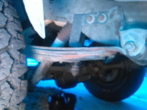 1992 Ford Bronco - Close-up view of the undercarriage, focusing on the leaf spring suspension system and a tire.