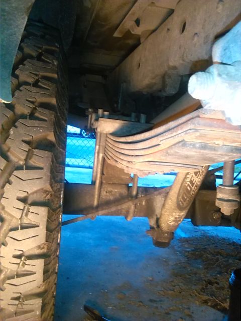 1992 Ford Bronco - Close-up of the rear suspension system and tire of a vehicle, showing leaf springs and a shock absorber.