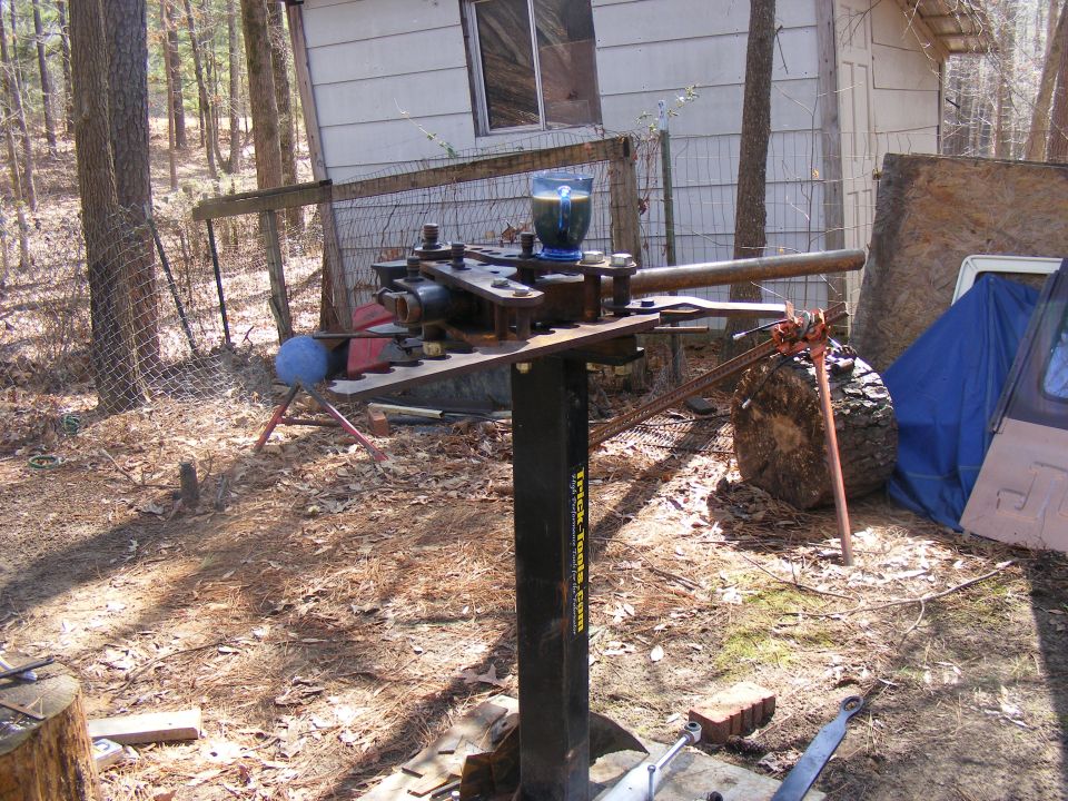 Pipe bender on stand, blue cup with drink on top, outdoors near shed