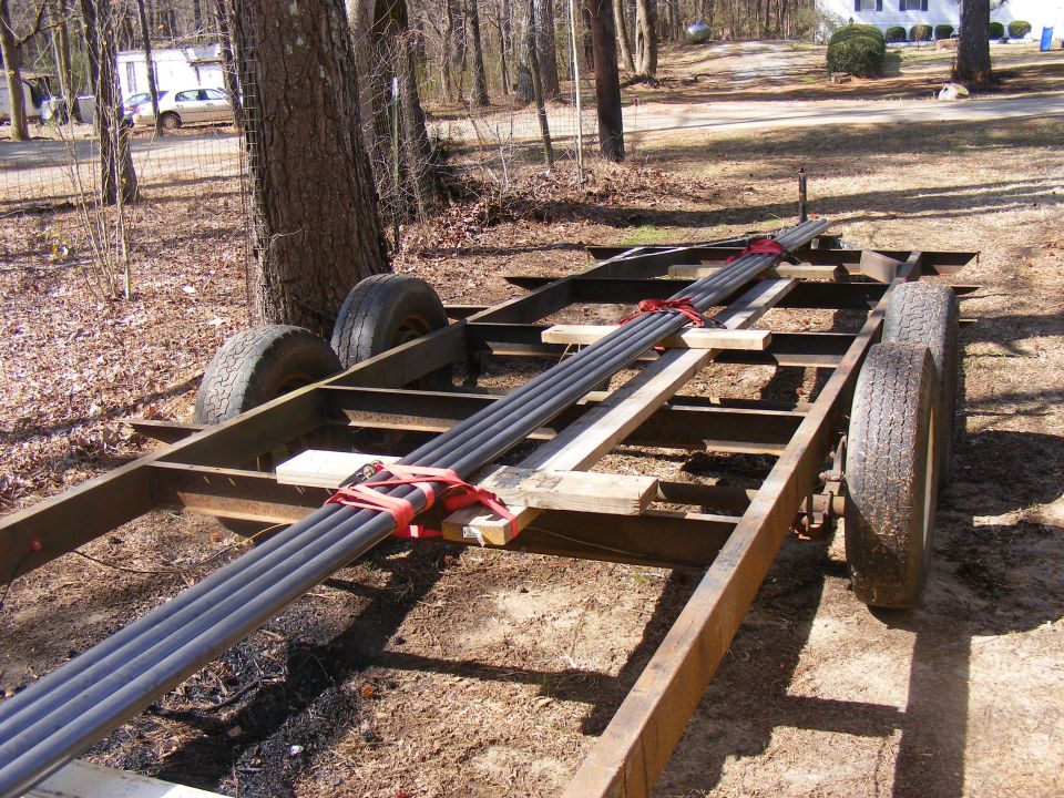 Trailer carrying pipes, strapped down. Trees and a house in background