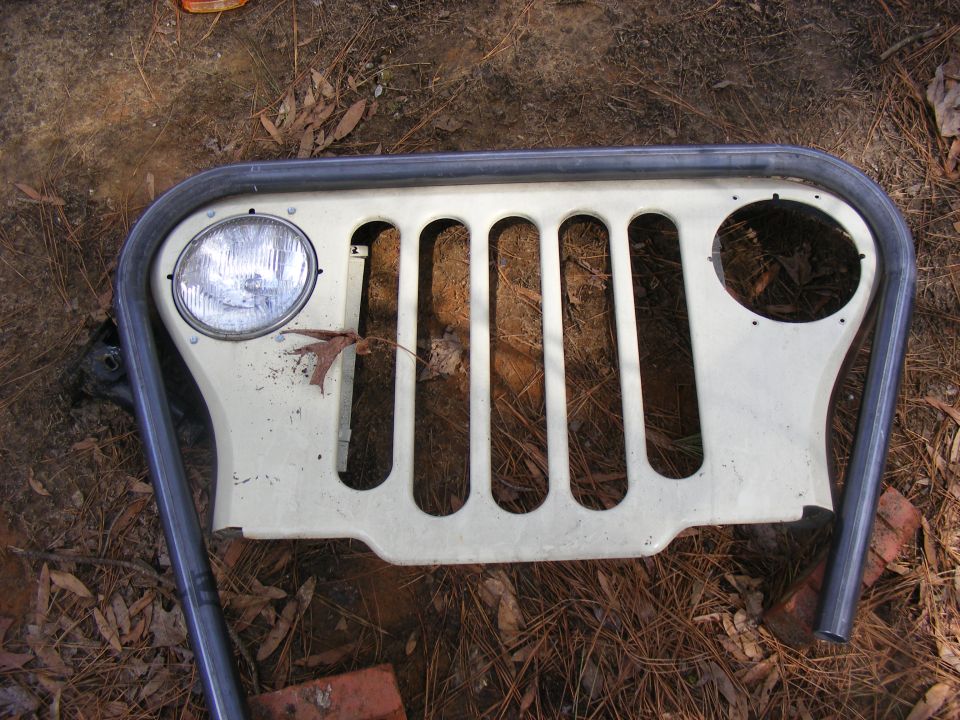 Cream-colored Jeep CJ grille with a chrome roll bar, lying on the ground