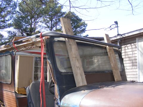 Side view of an old SUV with wooden planks propped against the windshield and a red strap on the roof rack