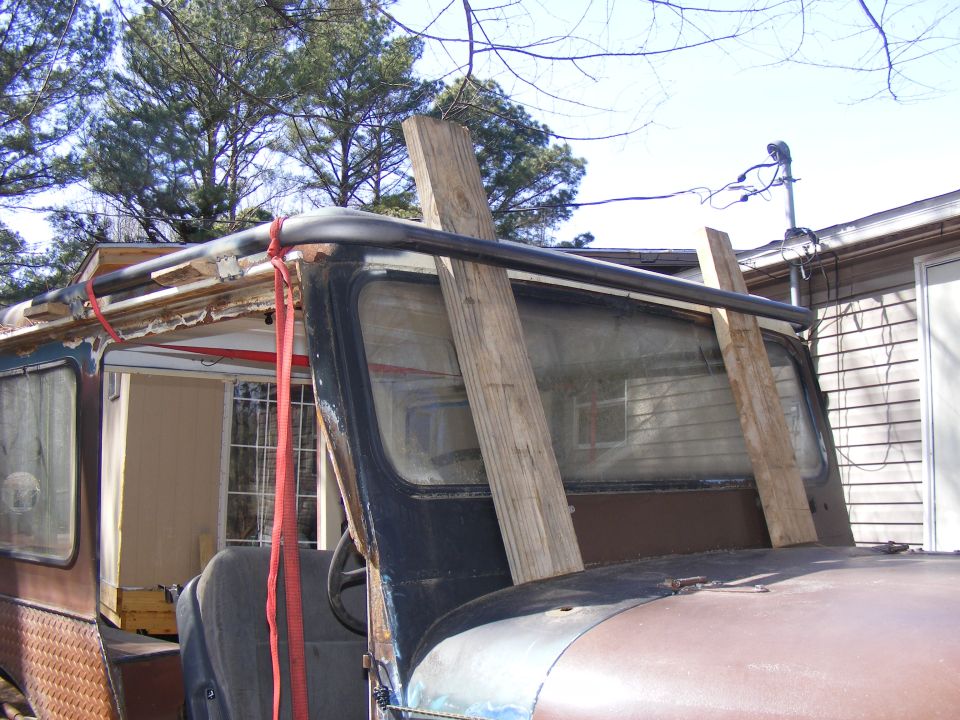 Side view of an old SUV with wooden planks propped against the windshield and a red strap on the roof rack