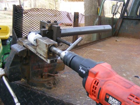 Drill with pipe held in vise on truck bed. Yellow tractor seat visible