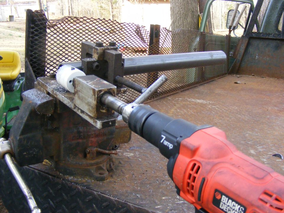 Drill with pipe held in vise on truck bed. Yellow tractor seat visible