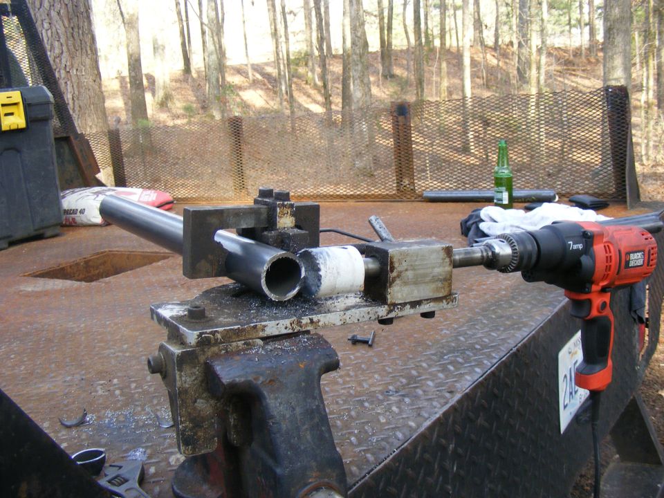Pipe held in vise with drill attached, on a trailer bed