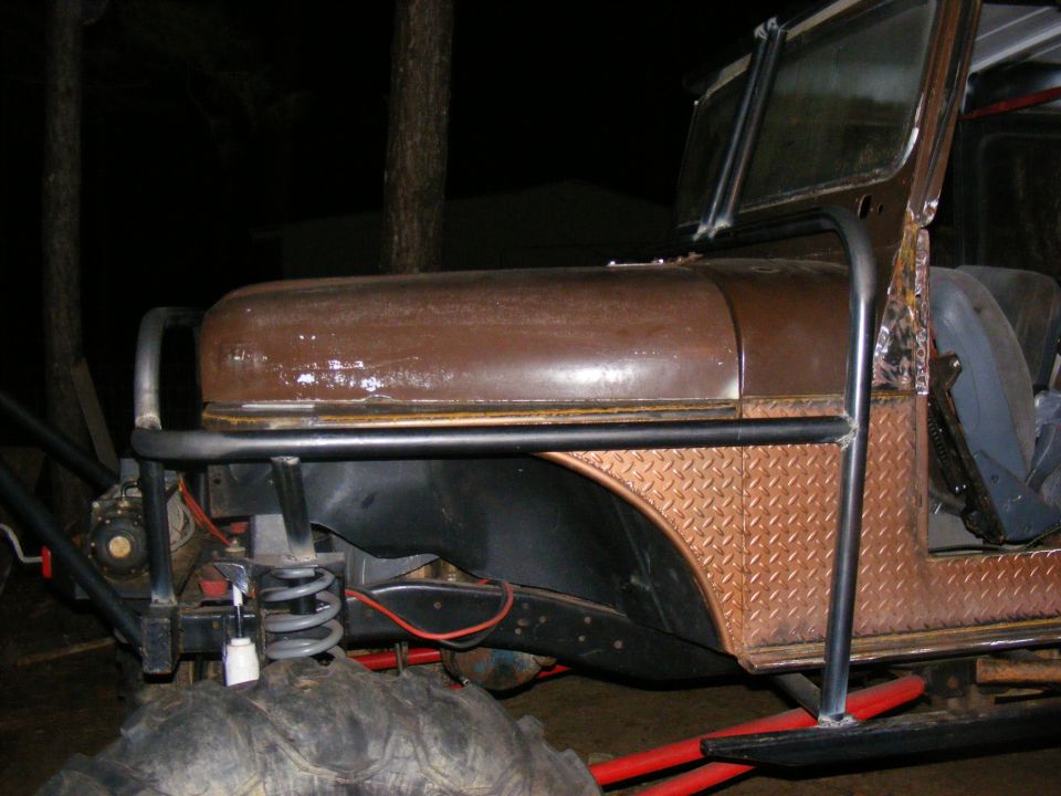 Brown off-road vehicle with diamond plate fender and large tires, viewed from the front quarter