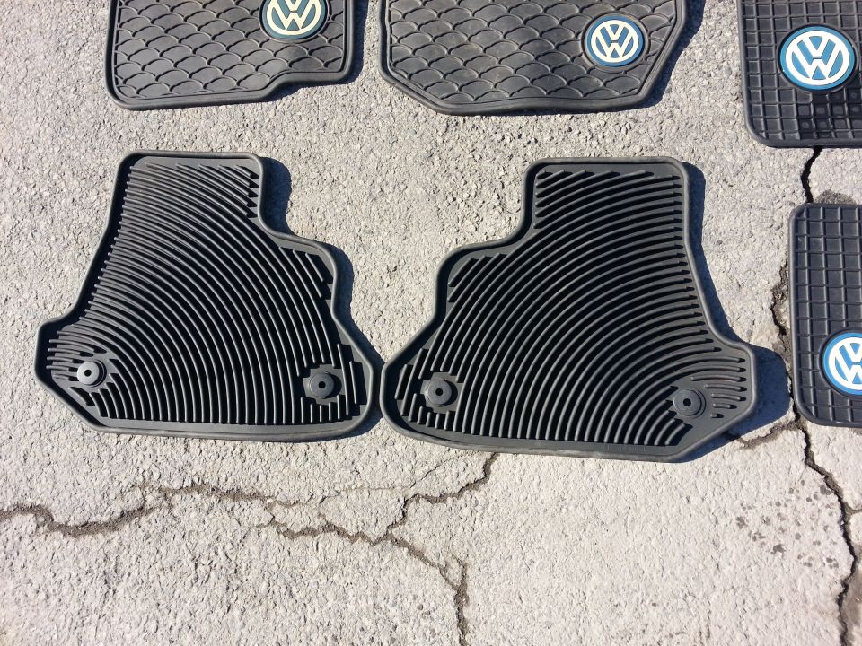 Several black rubber floor mats with Volkswagen logos on a concrete surface