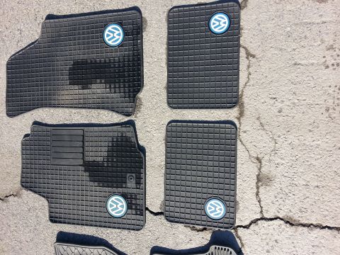 2002 Volkswagen Jetta - Set of four black rubber floor mats the Volkswagen logo, laid out on a cracked concrete surface.