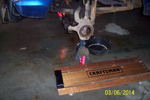 1973 Ford F-250 - Front axle assembly of a blue vehicle undergoing maintenance, supported by jack stands with an oil drain pan nearby.