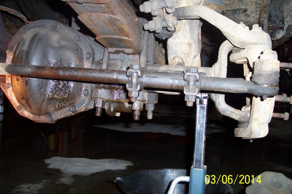 underneath view of a truck's rear axle, leaf springs, and steering linkage, supported by a jack