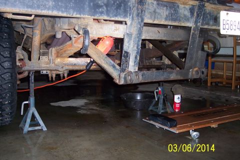 1973 Ford F-250 - The undercarriage of a 1973 Ford F-250 is visible, supported by jack stands, with leaf springs and frame components exposed.