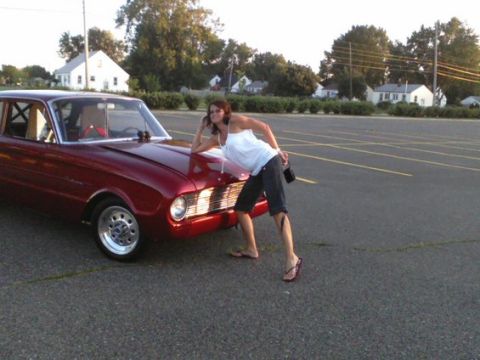 1960 Ford Falcon - Woman poses with a red 1960 Ford Falcon coupe in a parking lot.