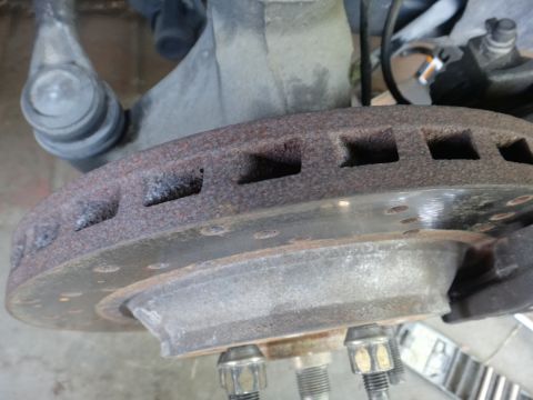 1993 Ford Taurus - A close-up view of a rusty vented brake rotor and associated suspension components.