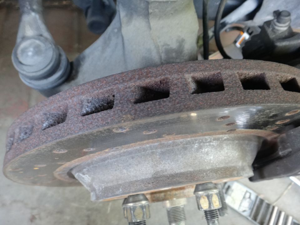 Rusty vented brake rotor with suspension parts. Close-up view