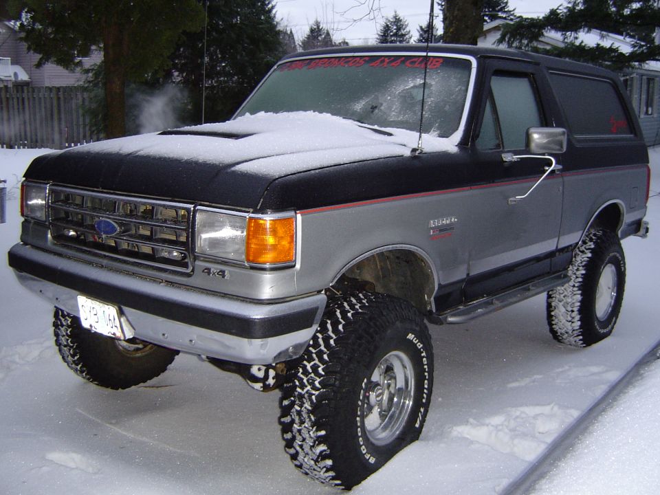 Lifted black-over-silver Ford Bronco on mud tires parked in snow, front three-quarter