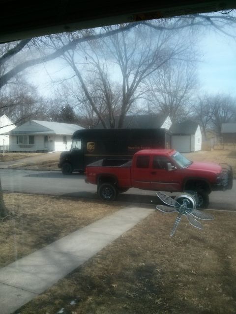 1986 Ford Bronco - A red pickup truck and a UPS delivery truck are parked on a street in front of houses.