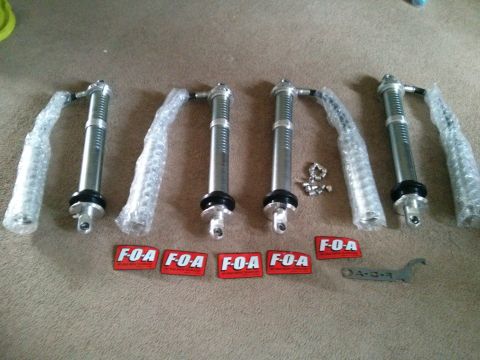 1986 Ford Bronco - Four F-O-A shock absorbers and a specialized wrench are laid out on a carpeted floor.