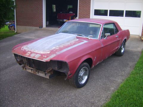 1968 Ford Mustang - This red coupe, likely a 1967 model, is missing its front grille and bumper, and has a custom hood scoop.