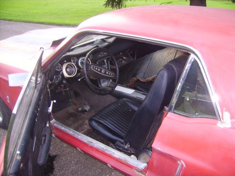 1968 Ford Mustang - The interior of a red 1968 Ford Mustang shows black vinyl seats and a dashboard with gauges.