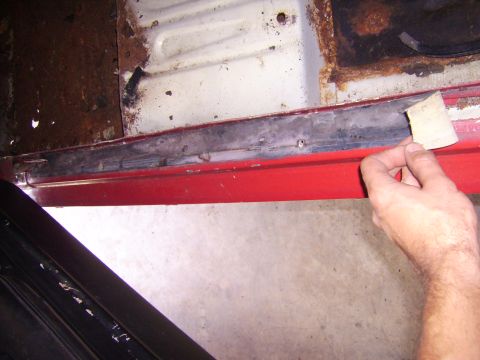 1968 Ford Mustang - A hand is shown sanding the rusty door sill of a vehicle, revealing red paint underneath.