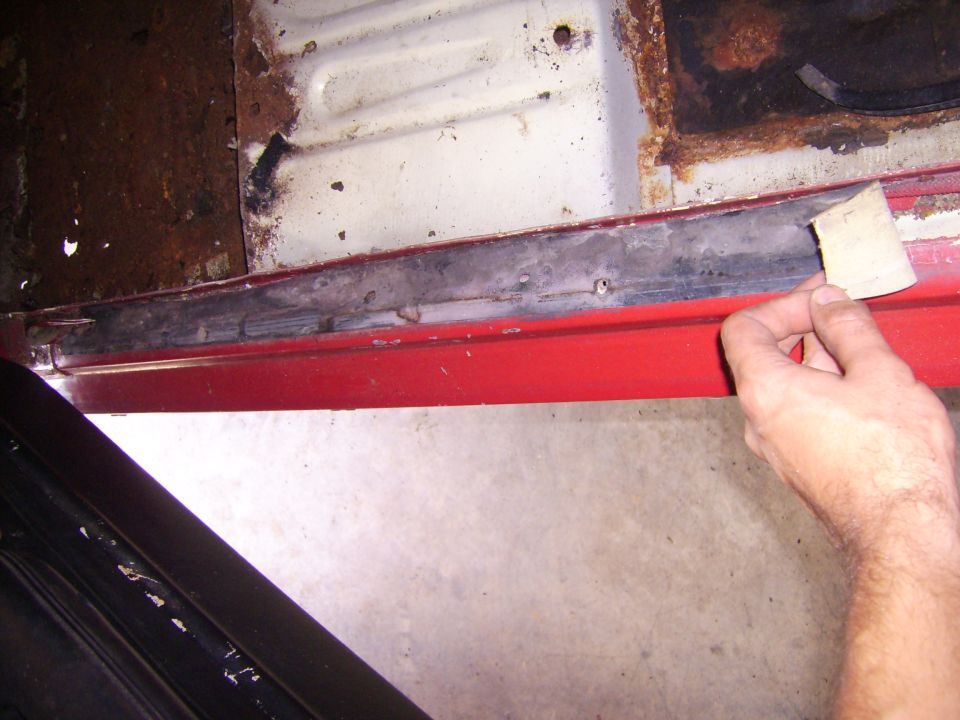 Hand sanding a rusty car door sill. Red paint visible below the sill