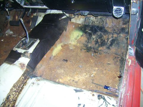 1968 Ford Mustang - The interior floor of a vehicle shows significant rust and deterioration, with a screwdriver lying on the damaged metal.