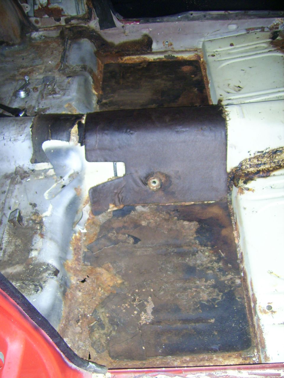 Car floor pan showing extensive rust damage and some torn upholstery
