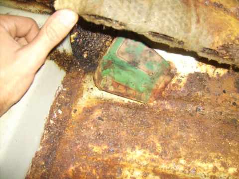 1968 Ford Mustang - A close-up view of severe rust damage on a vehicle's floor, with a green object obscured by the decay.