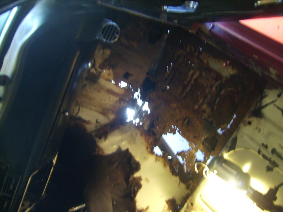 Interior view of a car's floor pan with extensive rust and holes