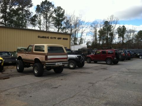 1988 Ford Bronco - A lifted Ford Bronco is parked outside a building labeled "Classic City Off Road" alongside other vehicles.